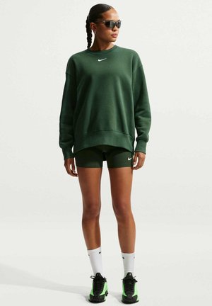 Sudadera verde de gran tamaño con un logo blanco, combinada con pantalones cortos verdes. Completado con calcetines blancos y zapatos negros con acentos neón.