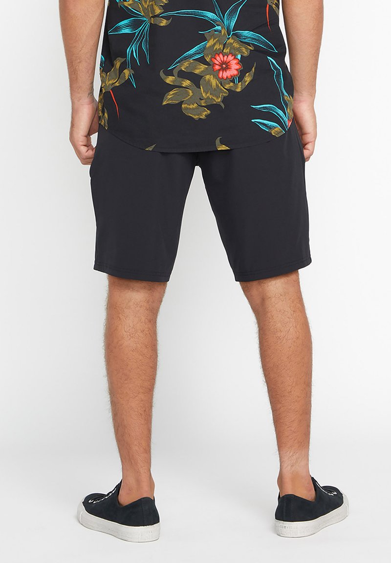 Black shorts in a relaxed fit, made of smooth fabric with an elastic waistband. Paired with a floral-patterned, short-sleeve shirt.