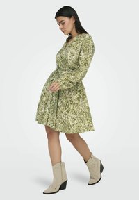 Groene jurk met een patroon, lange mouwen, een tailleriempje en een uitlopende rok. Gecombineerd met beige enkellaarsjes met een decoratief ontwerp.