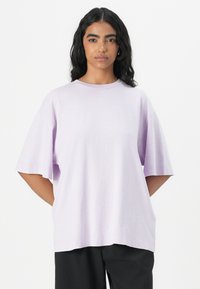 Tricou oversized de culoare mov deschis, realizat dintr-un material moale, având un decolteu rotund și mâneci scurte și largi. Croială casual și construcție laterală fără cusături.