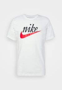 T-shirt bianco in cotone con un logo "nike" nero e un grafico Swoosh Nike rosso. Collo giro e maniche corte.