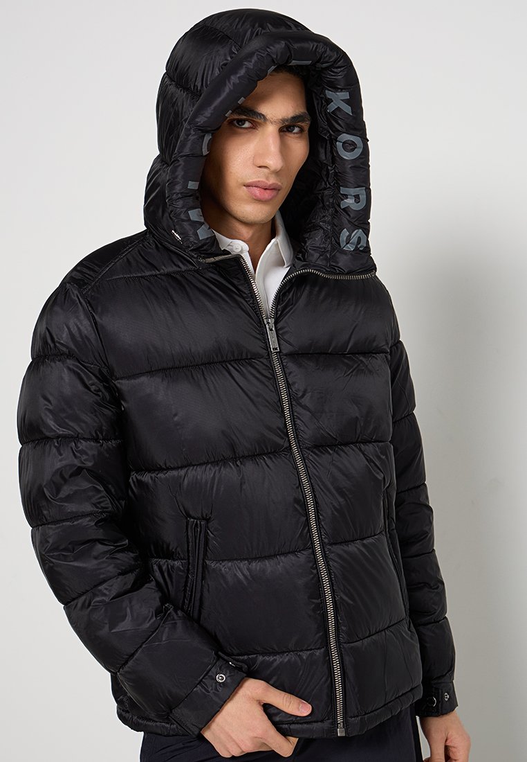 Giacca a vento nera con zip frontale, cappuccio e tasche laterali. Presenta una texture trapuntata e dettagli del logo all'interno del cappuccio.