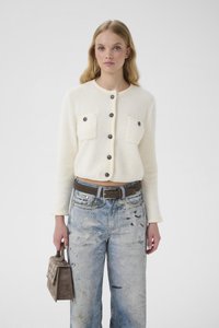 Krémově zbarvený krátký kardigan se dv�ěma předními kapsami a tmavými knoflíky, v kombinaci s modrými širokými kalhotami s podrápaným vzhledem a hnědou kabelkou.