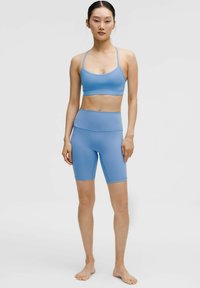 Gaiši zila aktīvās sporta apģērba komplekts, kas ietver bezšuvju sporta krūšturi ar plānām siksnām un augstām velosipēdu biksēm, abas izgatavotas no elastīga, gluda auduma.