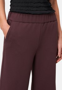 Bordeaux wijde broek van soepel materiaal, met een elastische tailleband en zijzakken, weergegeven met een zwart textuur top.