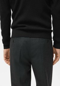 Black ribbed sweater with long sleeves, paired with gray check-patterned trousers featuring two back pockets and a button detail.
