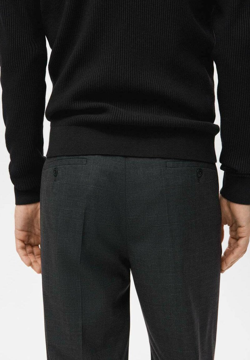Black ribbed sweater with long sleeves, paired with gray check-patterned trousers featuring two back pockets and a button detail.