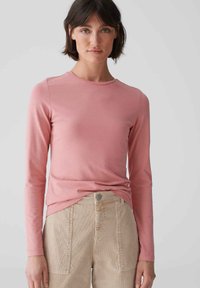 Langärmliges rosa Oberteil aus Baumwolle, mit Rundhalsausschnitt und taillierter Silhouette, kombiniert mit beigen Cordhosen.