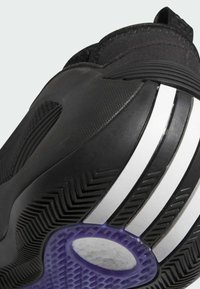 Scarpa da ginnastica nera con tomaia testurizzata, caratterizzata da strisce bianche e una suola in gomma viola con un motivo a zigzag per una migliore aderenza.