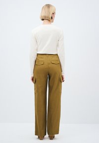 Khaki široké cargo kalhoty s několika kapsami a vysokým pasem, v kombinaci se smetanovým topem s dlouhým rukávem. Hladká textura, ležérní design.