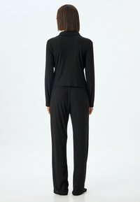 Conjunto de dos piezas de punto acanalado negro que incluye una chaqueta con cuello y pantalones a juego, ambos con un corte holgado y mangas largas.