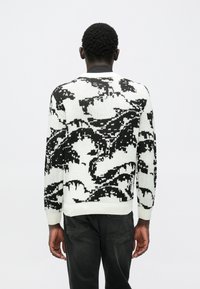 Gestrickter Pullover in Weiß und Schwarz mit einem abstrakten Muster. Rundhalsausschnitt, lange Ärmel und gerippte Bündchen mit entspannter Passform.