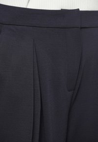 Marineblauwe broek van een gestructureerde stof, met een vlakke voorkant, geplooid design en een discreet zijvak.