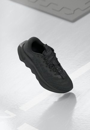 Chaussure de sport noire avec un upper en tissu texturé, semelle arrondie et un système de laçage complexe. Design minimaliste avec un logo subtil.