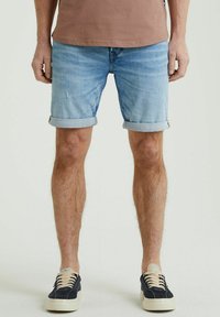 Shorts in denim blu chiaro con risvolti, caratterizzati da una leggera scoloritura e una vestibilità dritta, abbinati a sneakers scure e una camicia marrone.