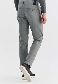 Szare, dopasowane spodnie o gładkiej fakturze, z tylnymi kieszeniami i detalem w postaci guzika. Połączone z czarnymi sneakersami i dopasowaną bluzką.
