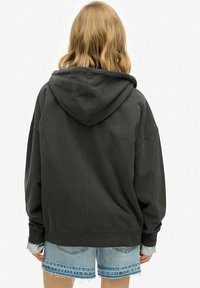 Sudadera gris oscuro con una gran capucha ajustable, corte relajado y puños acanalados, combinada con shorts de mezclilla azul claro con bordes deshilachados.