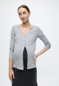 Γκρι ριγωτή ζακέτα με μακριά μανίκια, λαιμόκοψη V, με κουμπιά μπροστά, φορεμένη πάνω από μαύρο φόρεμα, με απαλό υλικό και εφαρμοστή σιλουέτα.