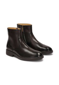 Botas negras de cuero hasta el tobillo con una textura suave, cierre lateral con cremallera y costuras mínimas sobre una suela de goma elegante.