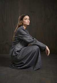 Grauer Blazer und passender langer Rock aus weichem, strukturiertem Stoff. Der Blazer hat eine schmale Form und Taschen; der Rock fließt bis zum Boden.