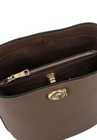 Interieur van een bruin leren handtas met een ritsvak, hardware in gouden tint en een gestructureerde afwerking. Heeft een drukknoopsluiting en voering.
