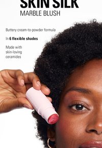 Krem-til-pulver blush-stick i lyserosa emballasje. Produktet viser en marmorert tekstur av myke rosa toner. Inkluderer hudvennlige ceramider.