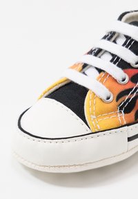 Zbliżenie na czubek sneakersów z białą gumową podeszwą, białymi sznurowadłami i kolorową tkaniną górną z pomarańczowymi i czarnymi wzorami.