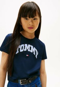 Marineblå kortærmet t-shirt med "TOMMY" logo i lyseblå, blødt stof, rund hals, som er parret med højtaljede denim og et sort bælte.