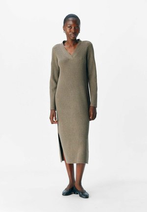 Robe en tricot vert olive avec un col en V et des manches longues. Présente une texture côtelée et une fente sur le côté à l'ourlet. Robe jusqu'au mollet.