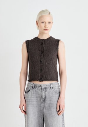 Gray sleeveless cropped top with a textured fabric, round neckline, and seven black buttons down the front. Worn with faded gray wide-leg jeans.