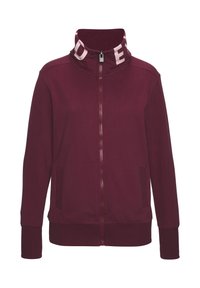 Bordeauxroter Reißverschlussjacke mit hohem Kragen und weißem Logo innen. Glatter Stoff, Seitentaschen sowie gerippte Bündchen und Saum.