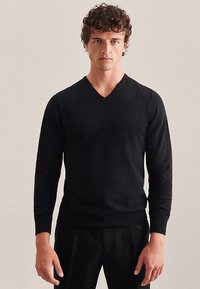 Schwarzer V-Ausschnitt-Pullover aus Strickmaterial mit langen Ärmeln und gerippten Bündchen, gezeigt an einem Modell vor neutralem Hintergrund.