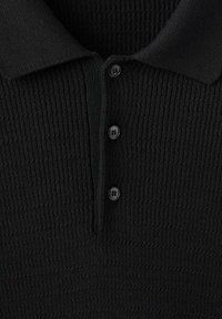 Polo negra con un diseño de texto acanalado, con un cuello clásico y tres botones a juego en el escote.