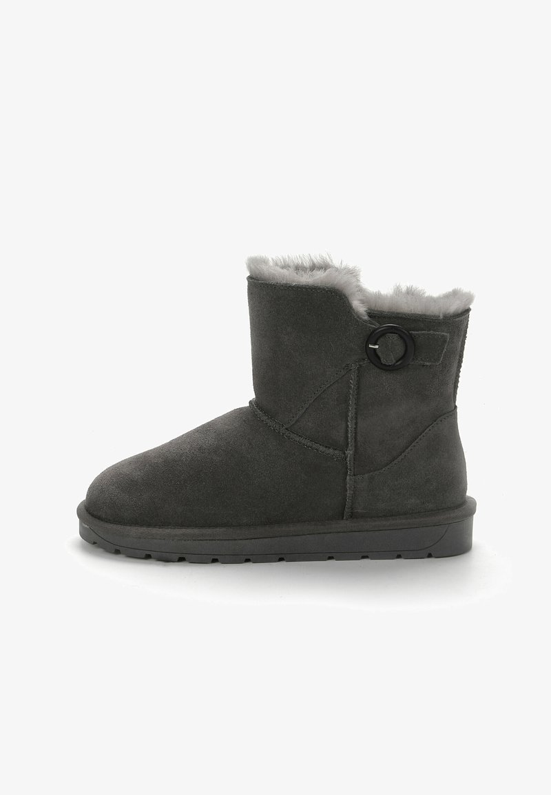 Bota de tobillo de ante gris con punta redondeada, forro de pelo gris suave y un botón circular negro decorativo en el lado. Suela de goma plana.