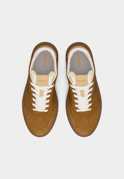 Paire de baskets en daim marron Versace avec lacets blancs et languette beige, vues de dessus sur un fond clair.