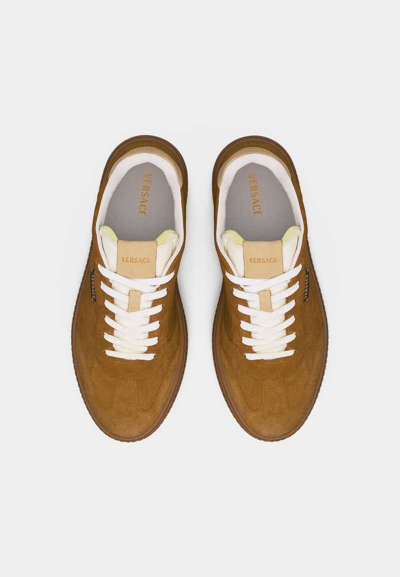 Paar brauner Veloursleder-Sneaker von Versace mit weißen Schnürsenkeln und beigefarbenem Zungenfutter, von oben auf einem hellen Hintergrund betrachtet.