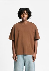 Brun oversized T-shirt i blød bomuld, med korte ærmer og rund hals. Subtil branding lige under halsudskæringen.