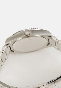Edelstahl-Uhr mit rundem Gehäuse, glattem Lünette, Krone und einem Gliederarmband. Die Rückseite ist flach und poliert mit eingravierten Details.