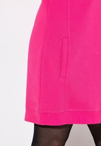 Vestido rosa fucsia con una textura suave, que presenta un bolsillo lateral oculto y un dobladillo acanalado. El diseño es ajustado y ligeramente por encima de la rodilla.