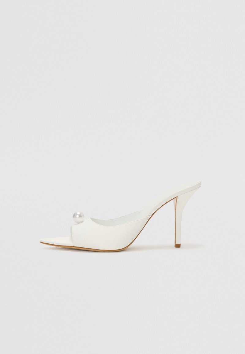 Pantof alb cu toc deschis, cu vârful ascuțit, finisaj neted și un accent decorativ din perlă pe lateral. Toc subțire de tip stiletto și design minimalist.
