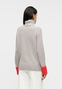 Ανοιχτό γκρι πουλόβερ με ζιβάγκο και κόκκινες ριγωτές μανσέτες. Απαλό, υφασμάτινο με υφή πλεκτό, με άνετη εφαρμογή και σκίσιμο στη φάσα πίσω.