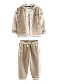 Ensemble sweat-shirt beige et pantalon de jogging assorti. Le sweat-shirt présente une ouverture à boutons, des accents de poches et des poignets rayés blancs. Mélange de coton doux.
