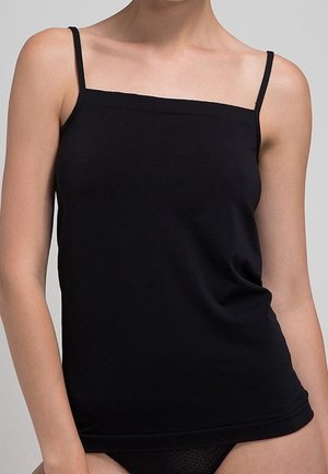 Vrouw draagt een aansluitend zwart mouwloos hemdje met dunne bandjes en een vierkante halslijn tegen een neutrale achtergrond.