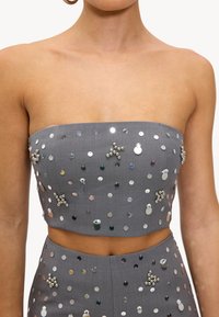 Haut court gris sans bretelles orné de sequins et de perles disposés de manière éparse sur toute la surface. Tissu lisse, coupe ajustée.