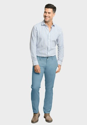 Camisa de botones a rayas azul y blanca combinada con pantalones celestes y zapatos marrones. Presenta mangas largas y botones frontales.