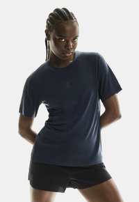 Tengerészeti edzőpóló könnyű, lélegző anyagból. Kerek nyakkivágással és rövid ujjakkal rendelkezik, fekete rövidnadrággal párosítva.