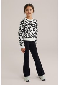 Čierno-biely sveter s kvetinovým motívom a skráteným strihom, doplnený o čierne kordrové zvonové nohavice a svetlé tenisky.