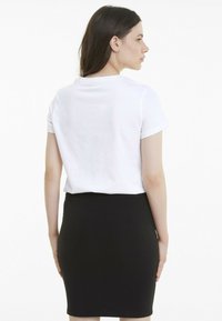Biała bawełniana koszulka z krótkim rękawem, zestawiona z czarną dopasowaną spódnicą; oba elementy charakteryzują się prostym, klasycznym wzornictwem i gładką teksturą.