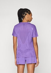 Camiseta deportiva morada con un patrón texturizado, mangas cortas y acentos reflectantes, acompañada de pantalones cortos a juego.
