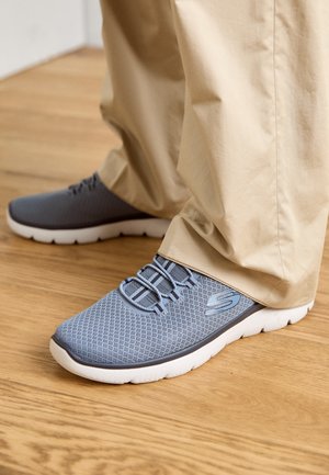 Adidași gri deschis cu un branț din plasă respirabilă, având șireturi elastice, o talpă groasă albă și un accent cu logo pe lateral.